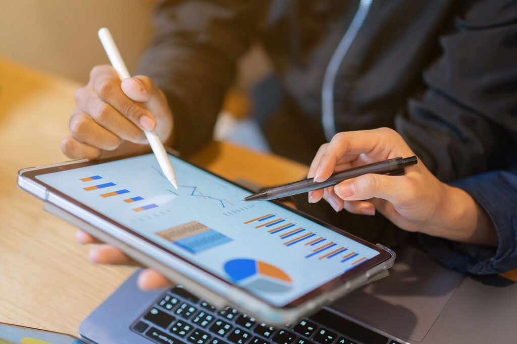 People writing on a tablet displaying charts and graphs, showing the admin required for effective debt recovery that is simplified with Debt Tec.